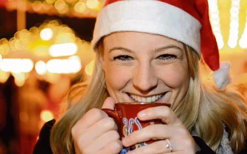 Blonde Frau im Portrait mit Weihnachtsmütze trinkt Glühwein