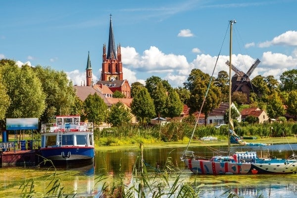 Havelland mit grünem See, Schiffen und einer roten Kirche im Hintergrund